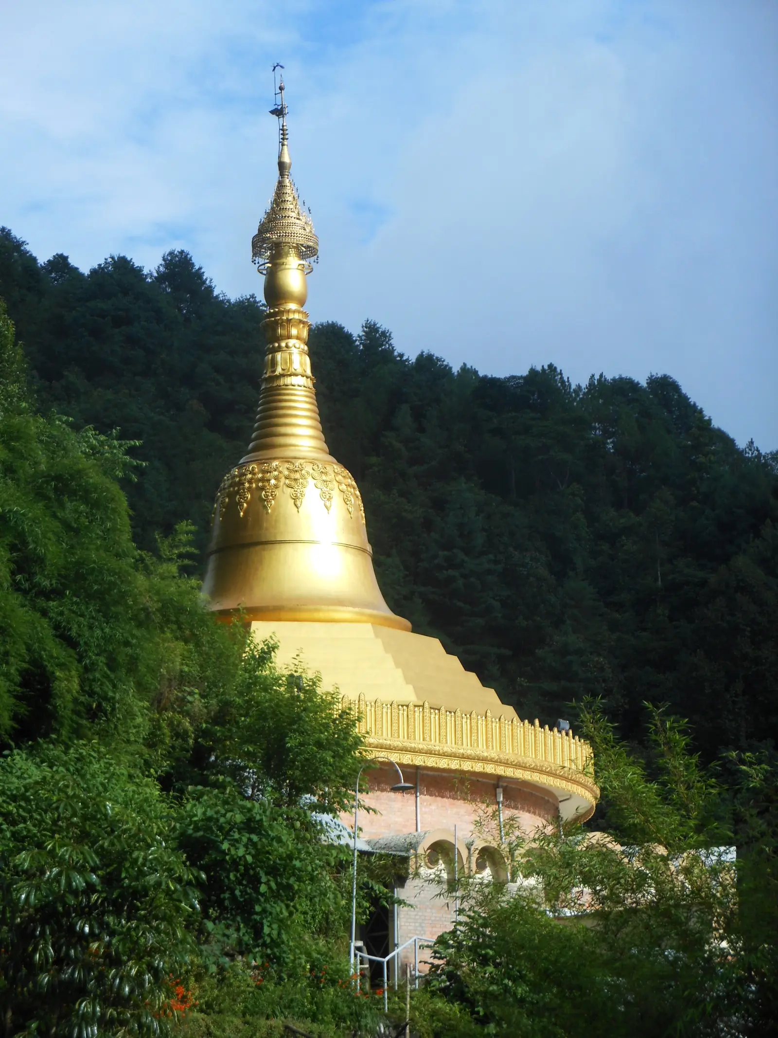 The golden pagoda of Dhamma Shringa rising among green forest on the hillside above Budhanilkantha, Kathmandu
