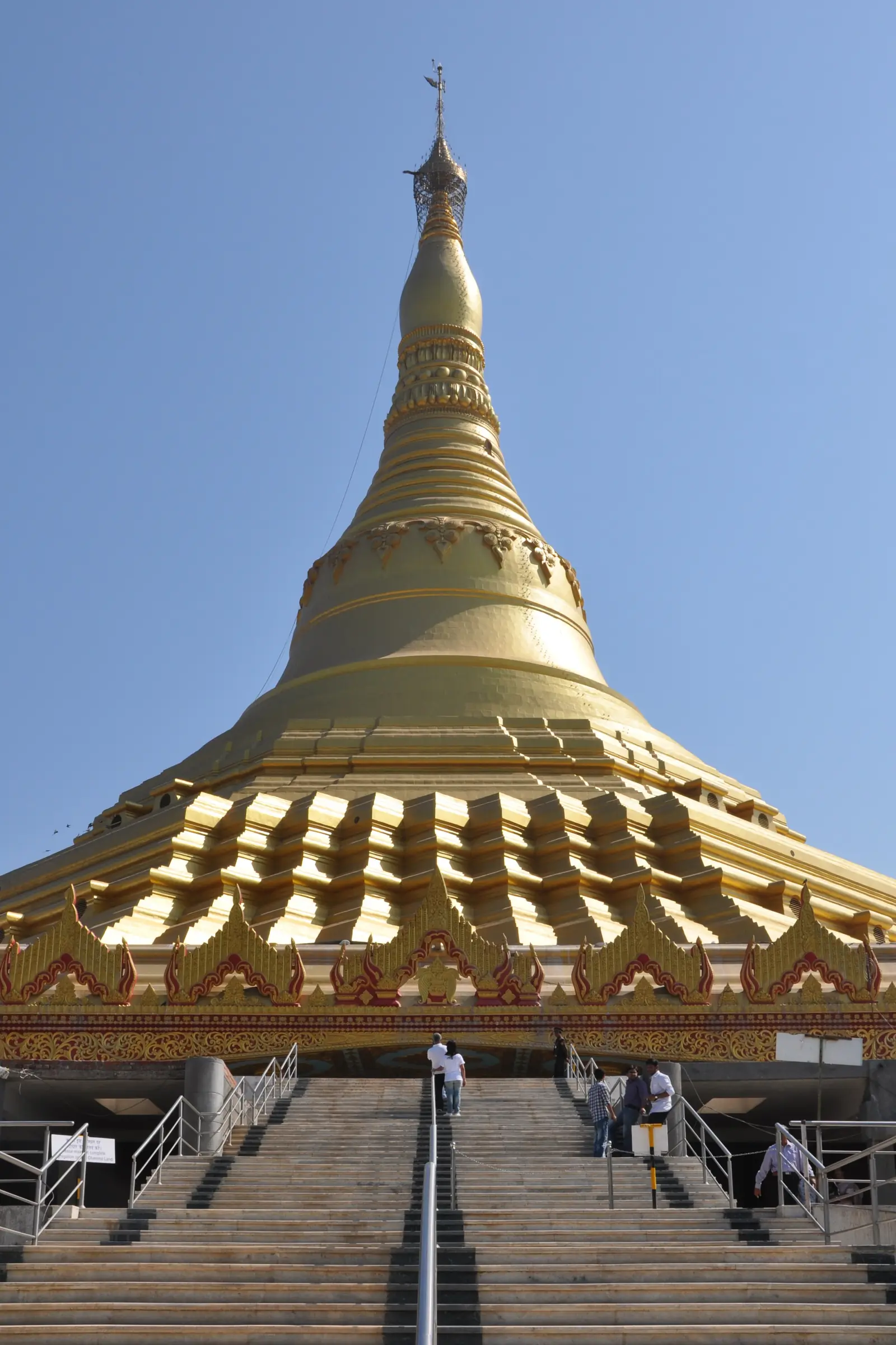 The gilded spire of the Global Vipassana Pagoda rising above its entrance stairway against a clear blue sky
