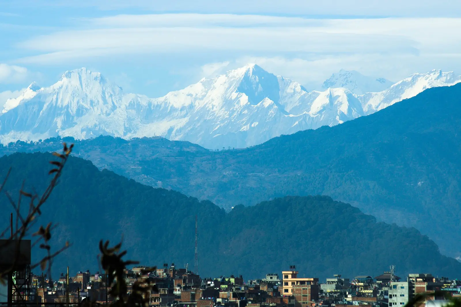 Snow-covered peaks of the Ganesh Himal rising above layered blue foothills and the rooftops of the Kathmandu valley