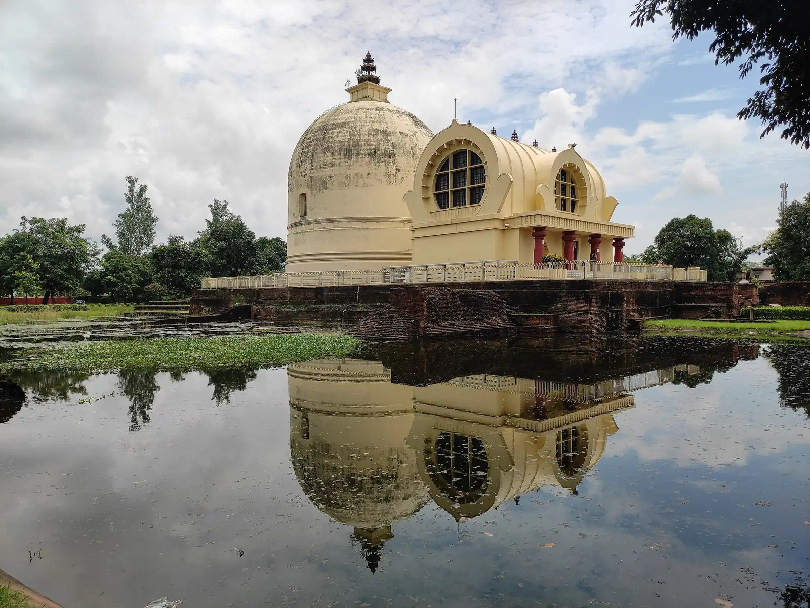 The cream-coloured Parinirvana stupa and Mahaparinirvana Temple at Kushinagar reflected in a still pond