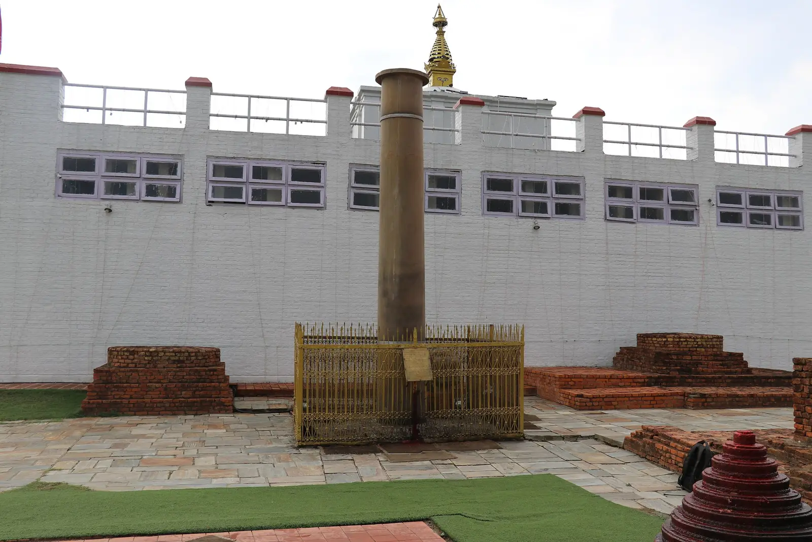 The sandstone Ashoka pillar inside a low golden railing in front of the white Maya Devi Temple, Lumbini