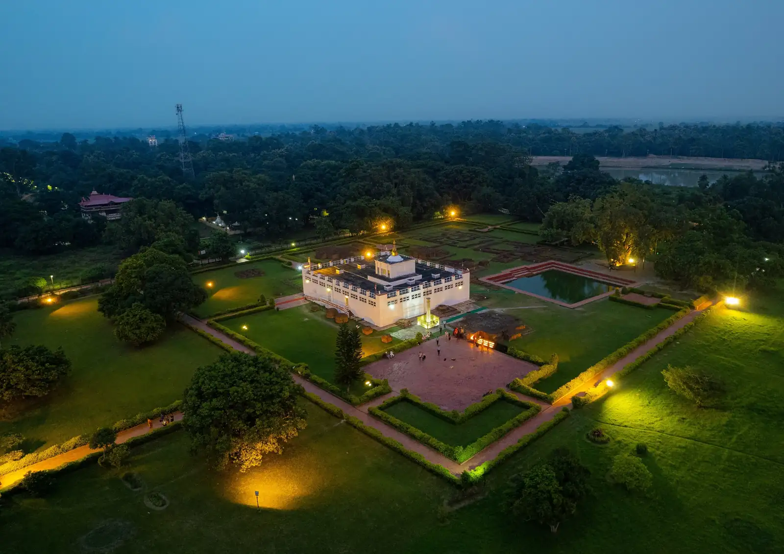 Aerial view at dusk of the Lumbini sacred garden, with the lit Maya Devi Temple, the sacred pond and paths surrounded by trees