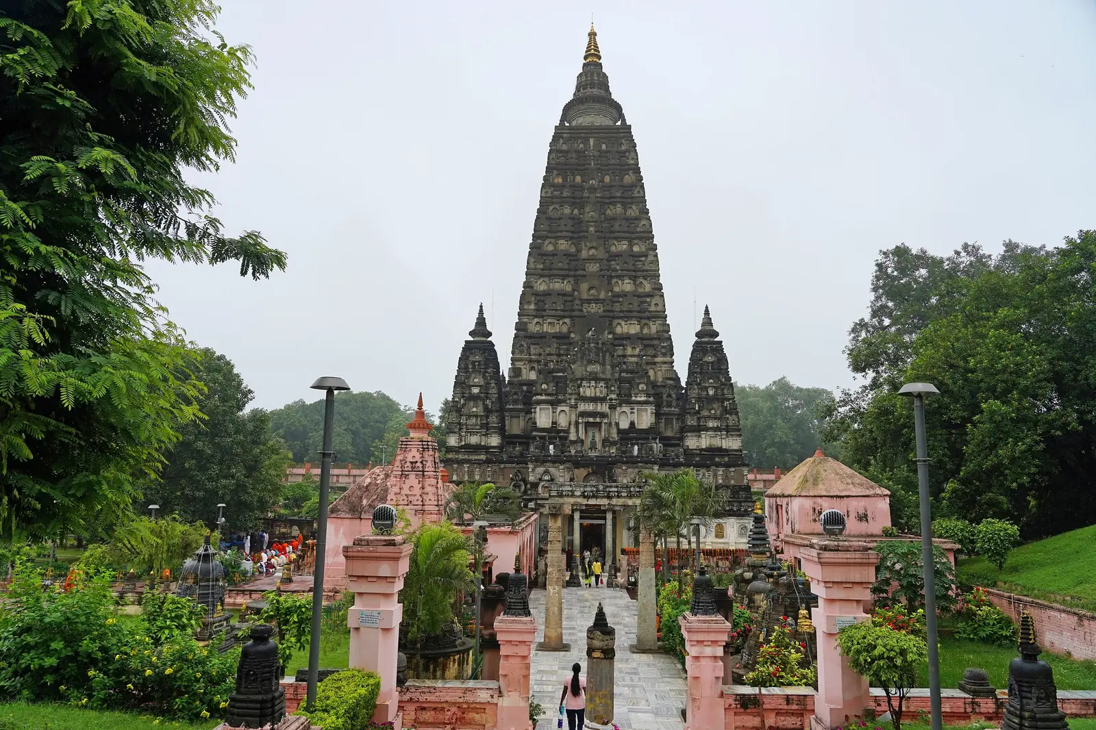 The tall pyramidal tower of the Mahabodhi Temple at Bodh Gaya rising above gardens and a path leading down to its entrance