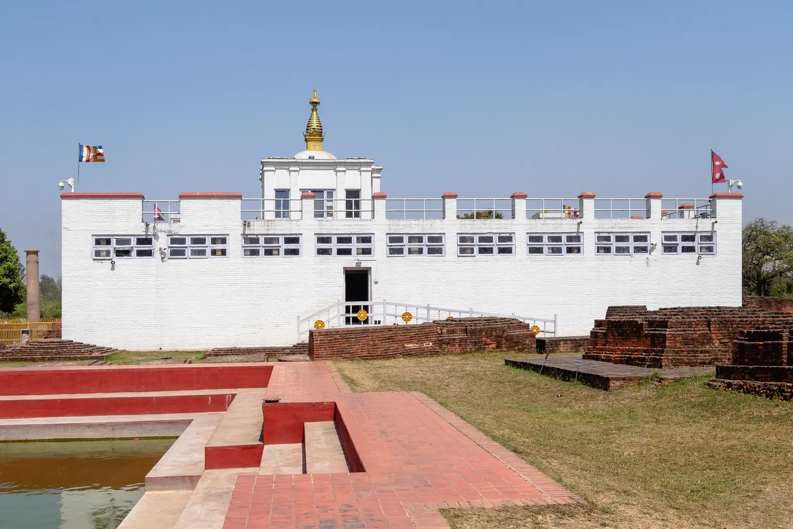 Front view of the white Maya Devi Temple in Lumbini with red-brick steps and ancient brick foundations in the foreground