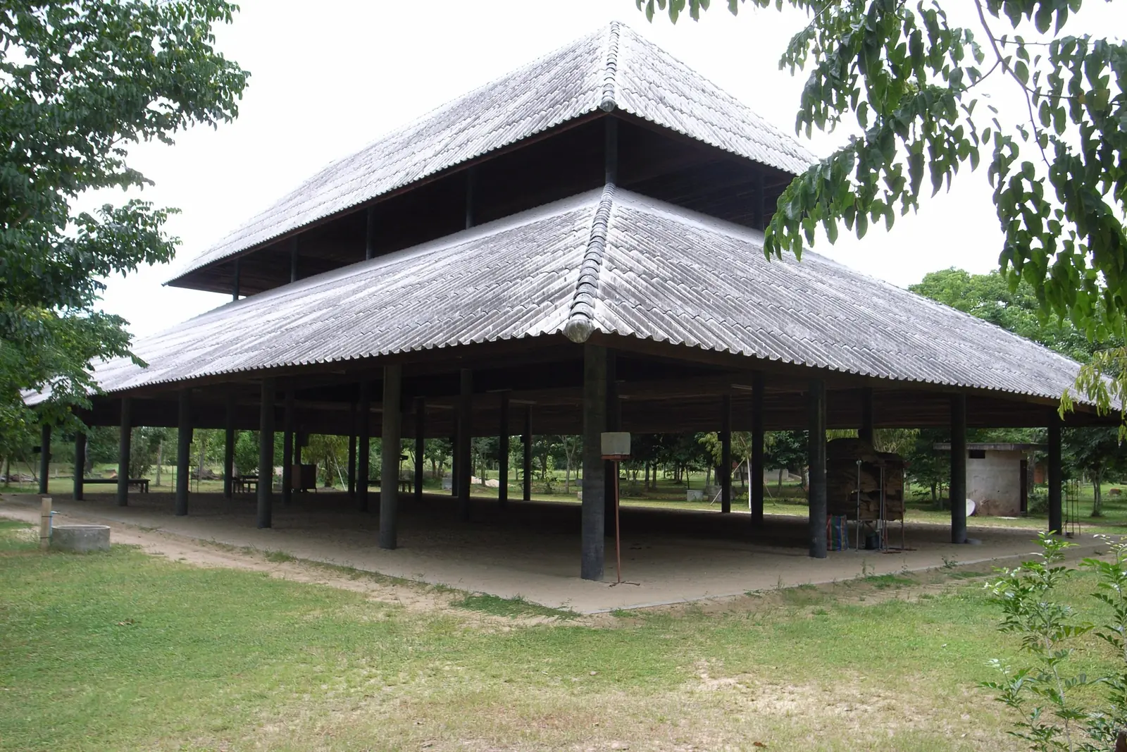 An open-sided wooden meditation pavilion with a double-tiered roof on a lawn among trees at Suan Mokkh