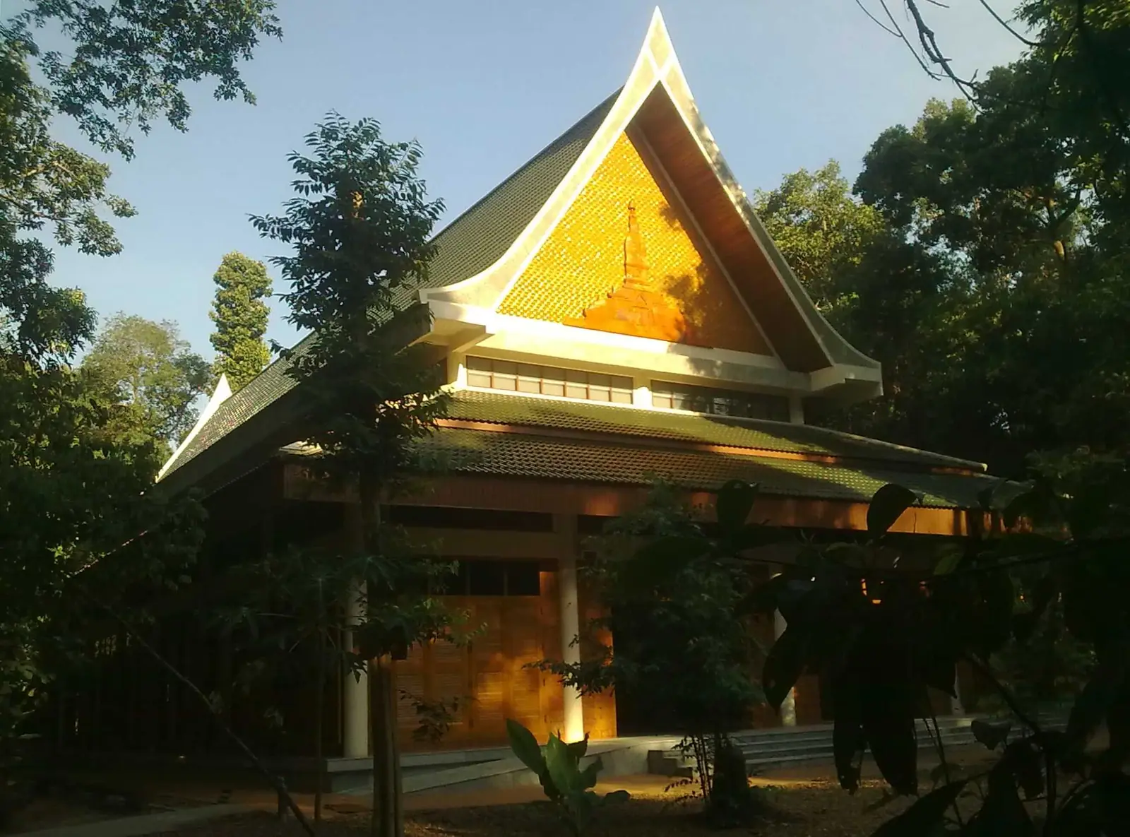The wooden meditation and Dhamma hall of Wat Pah Nanachat with a steep Thai-style roof and golden gable, surrounded by forest trees