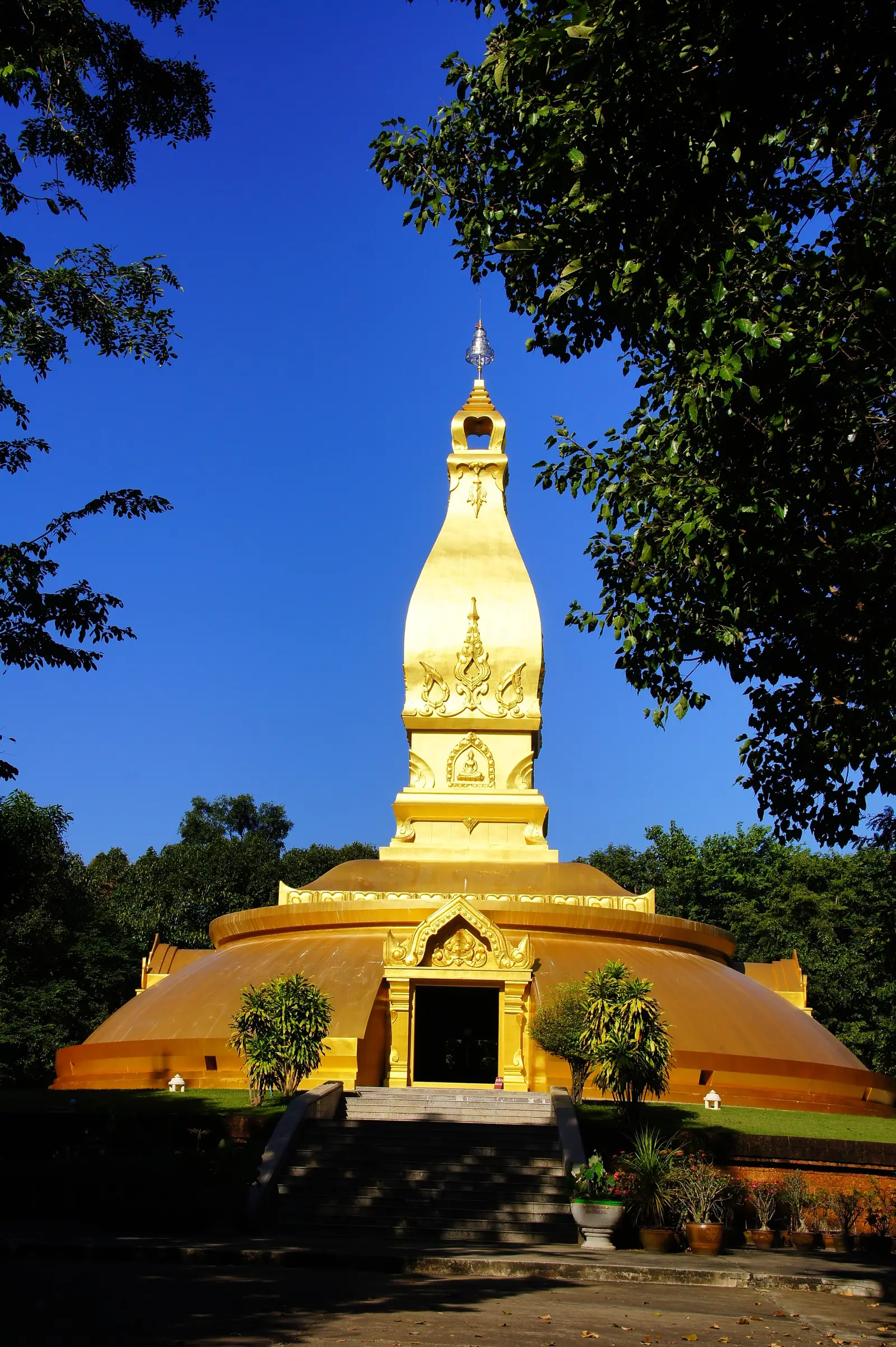 The golden memorial chedi of Ajahn Chah at Wat Nong Pah Pong rising against a deep blue sky between forest trees