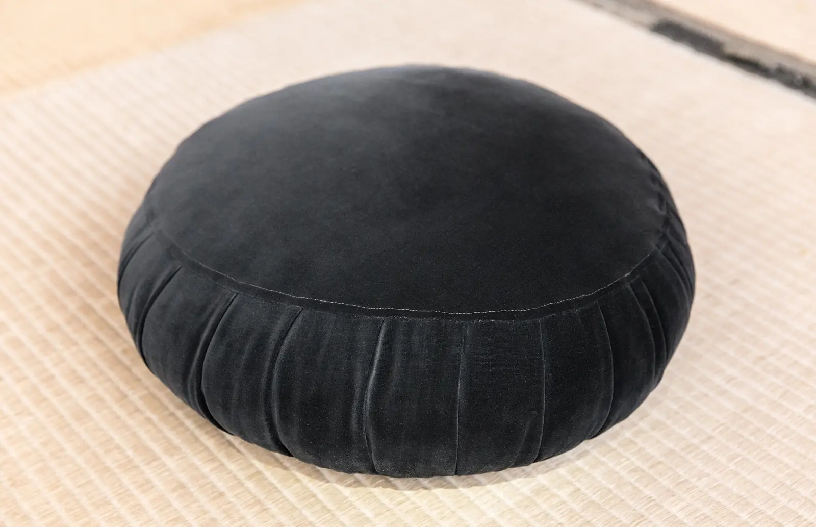 A single round black pleated meditation cushion resting on a pale tatami mat