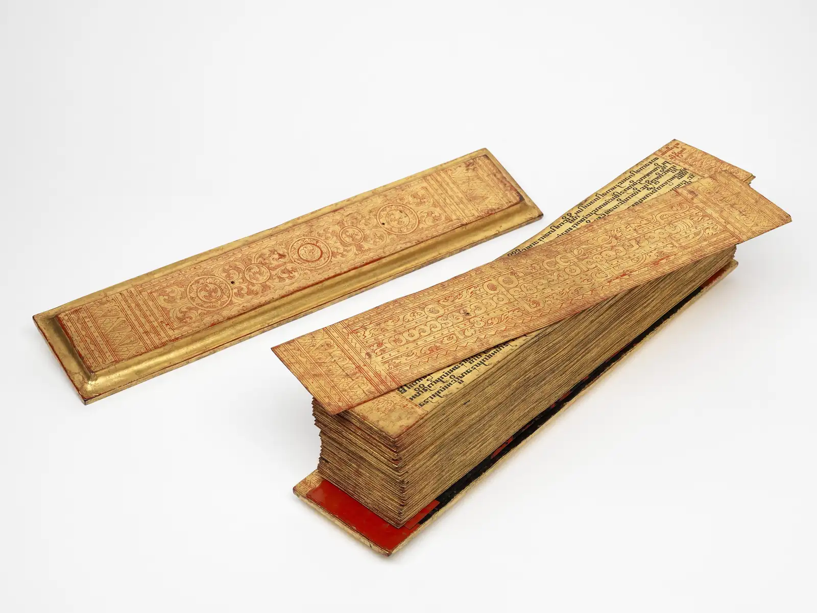 A Burmese Pali manuscript: a stack of gilded palm leaves between decorated gilt wooden covers, photographed on a white background