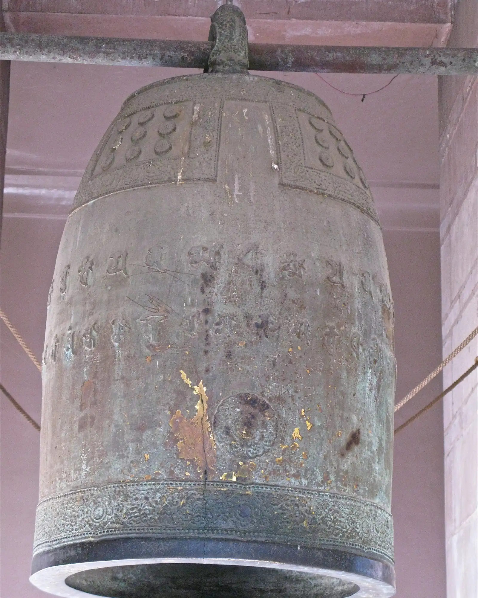 A weathered bronze temple bell with raised inscriptions hanging from a beam