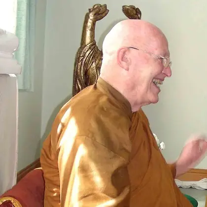 Ajahn Sumedho, an elderly Western monk in ochre robes and glasses, laughing