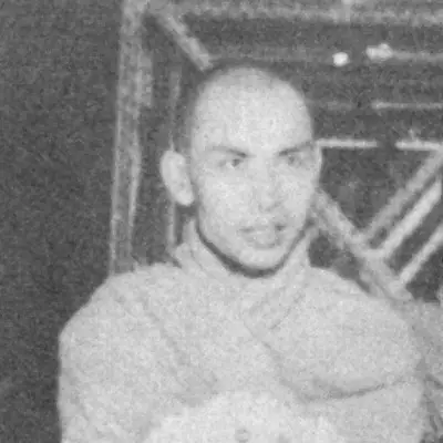 Grainy black-and-white photograph of the young monk Amritananda, shaven-headed and wearing a robe, seated among other monks