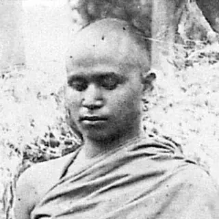 Black-and-white photograph of the young monk Mahapragya, shaven-headed with eyes lowered, wearing a robe over both shoulders, outdoors