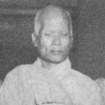 Grainy black-and-white photograph of the elderly monk Pragyananda, with close-cropped grey hair and a pale robe, seated
